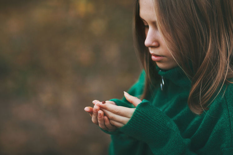 Beautiful blonde teenage girl in a warm green sweater with a ladybug in an autumn park.