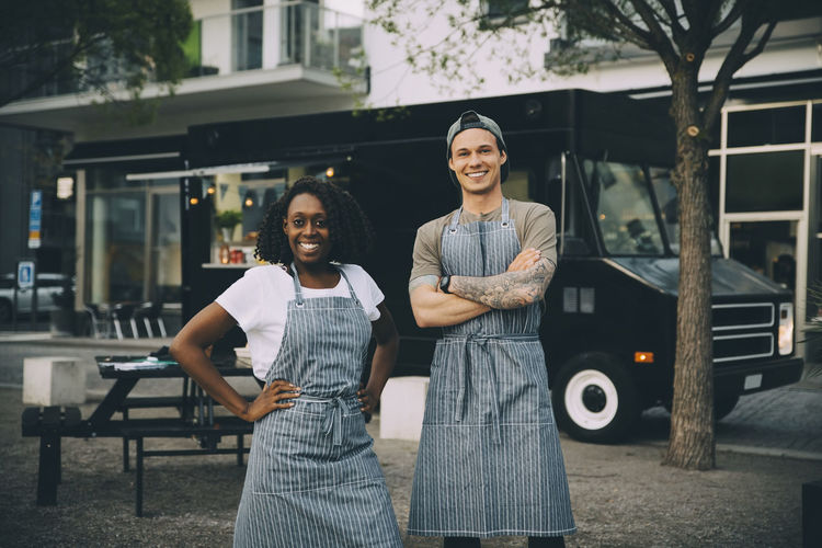 Portrait of smiling male and female owners standing against food truck in city