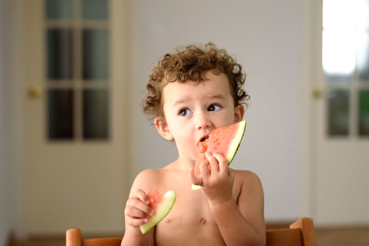 Portrait of shirtless boy eating fruit at home