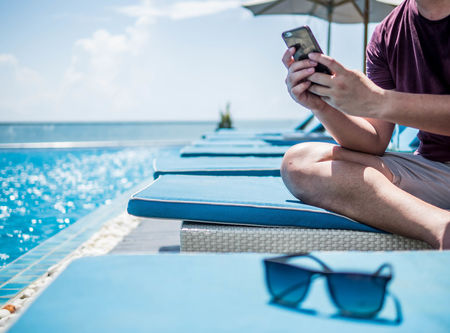 Midsection of man using smart phone while sitting by swimming pool