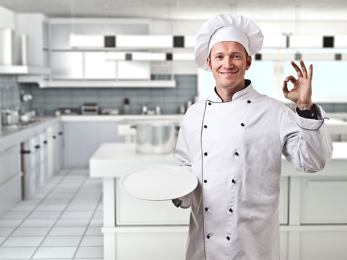 Portrait of male chef smiling while gesturing ok sign in kitchen