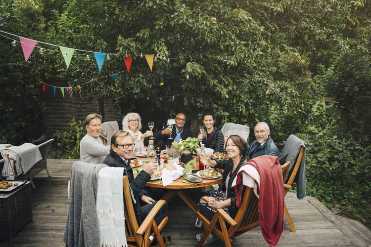 Portrait of smiling active senior men and women with celebratory toast sitting at dining table at back yard during party