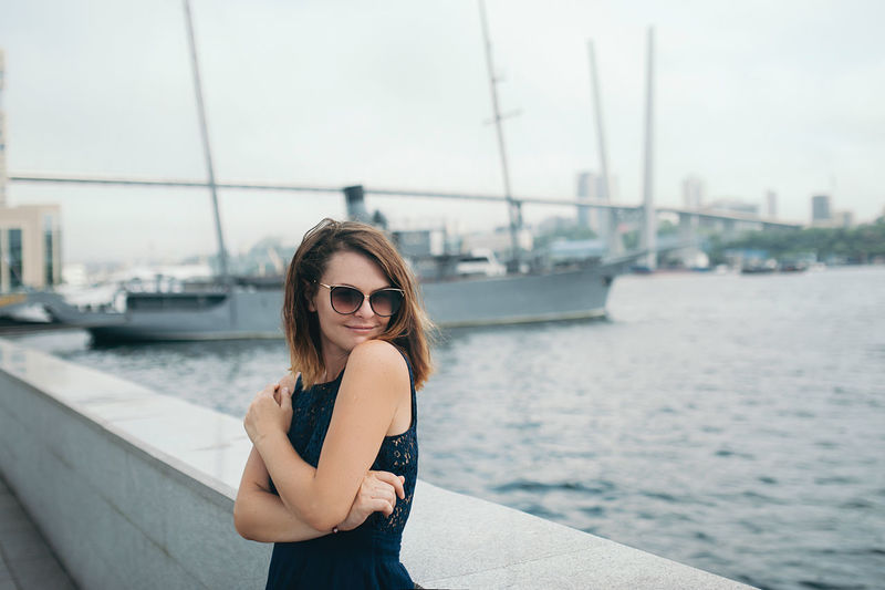 Beautiful brunette girl in a blue dress and sunglasses in the port, ship and cable-stayed bridge