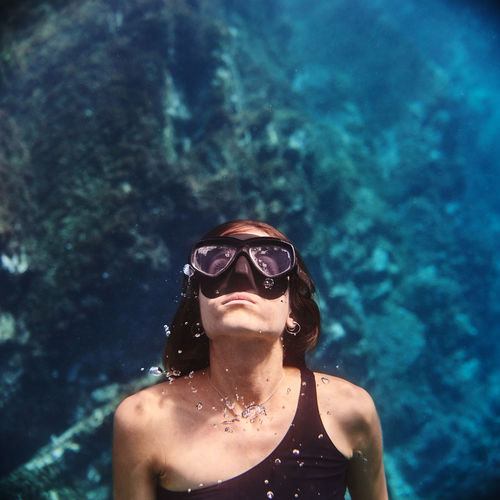 Young female diver in swimsuit and snorkeling mask floating in clean transparent sea water