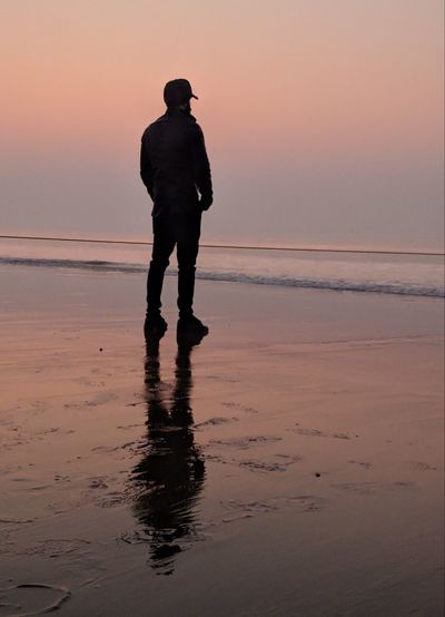 Rear view full length of man standing at beach during sunset