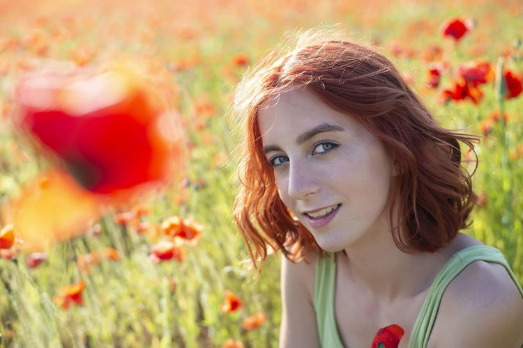 Portrait of beautiful young woman standing amidst flowering plants on field