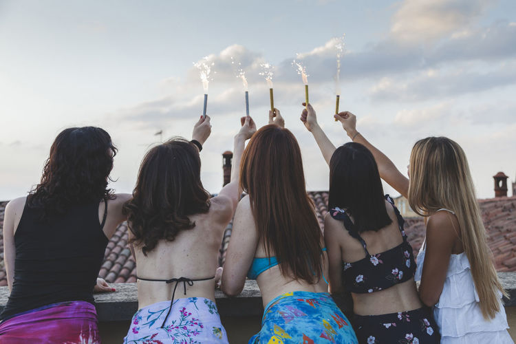 Rear view of female friends holding sparklers against sky