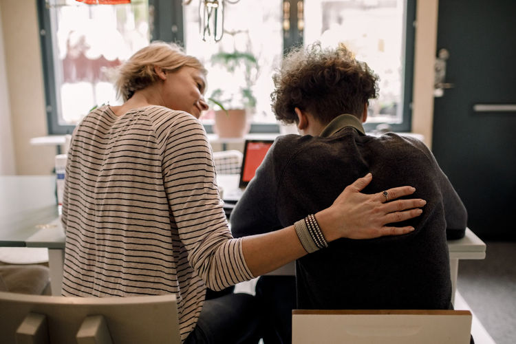 Mother sitting by teenage son studying at home
