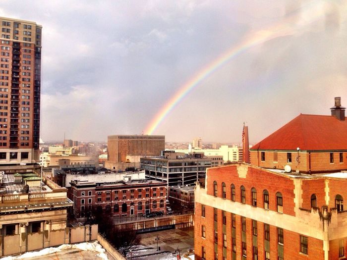 Rainbow over city against cloudy sky