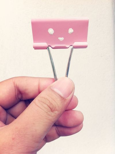 Cropped image of hand holding paper clip against white background