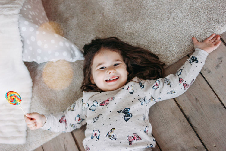 High angle portrait of happy girl with candy lying on floor
