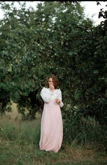 Portrait of woman biting fruit while standing against plant