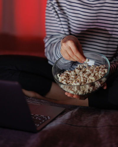 Woman in a striped sweatshirt and hat eats popcorn and watches a movie on tv or a tv series at