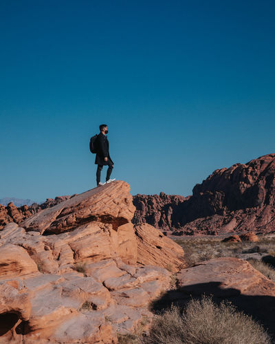 Man standing on rock against clear blue sky