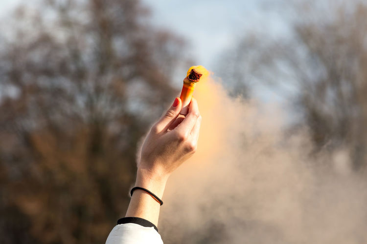 Cropped hand of woman holding distress flare against sky