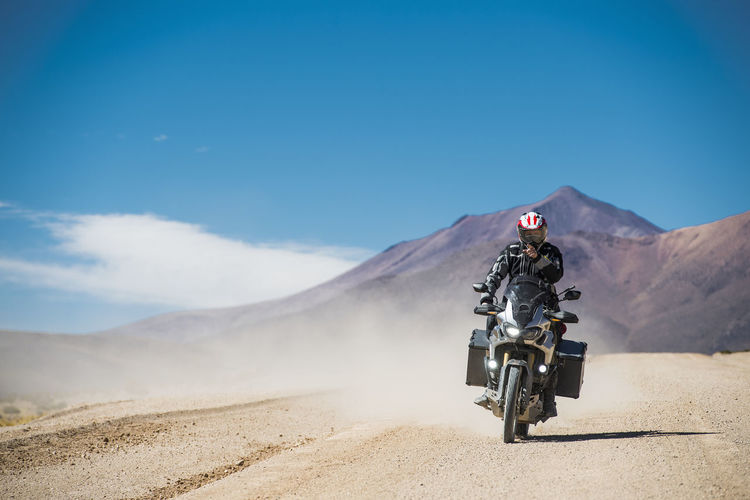 Man riding motorcycle on desert against sky