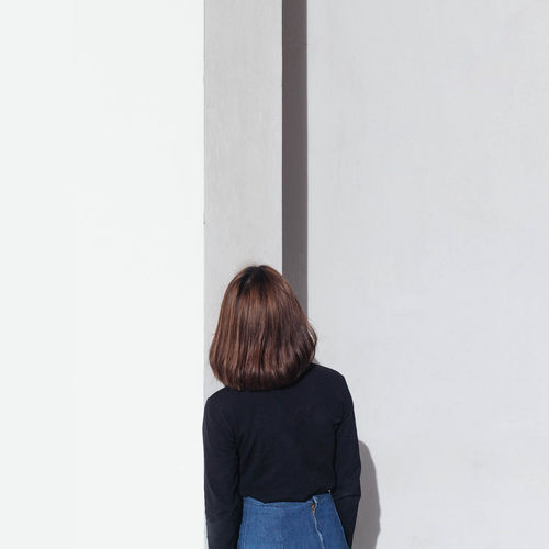 Rear view of woman standing against white wall