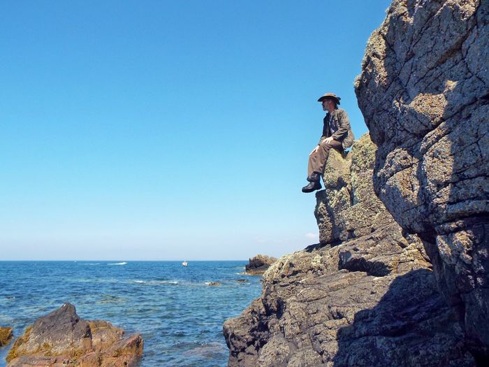 Man rock on sea against clear blue sky