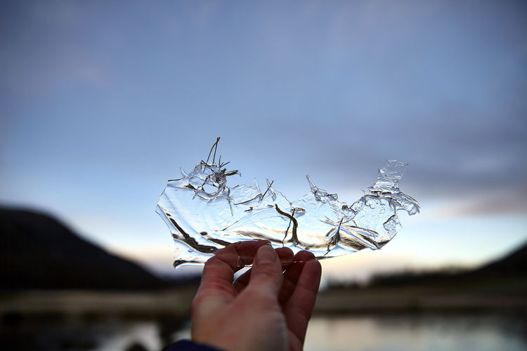 Close-up of hand holding glass against sky