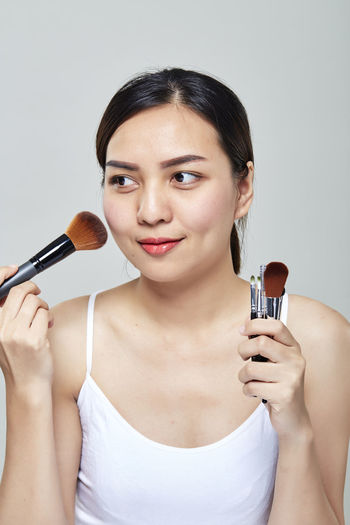 Beautiful mid adult woman applying make-up over gray background