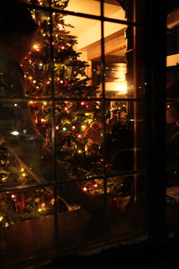 Illuminated christmas tree seen through glass window at night