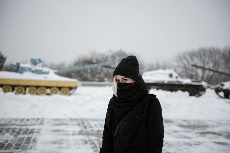 Portrait of young woman with obscured face standing on snow covered landscape against sky