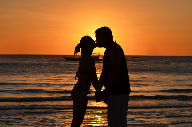 Silhouette couple kissing while standing on shore at beach during sunset
