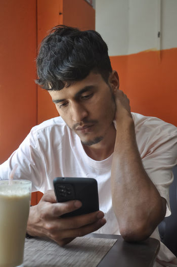 Close-up shot of a young guy using his phone while sitting in cafe