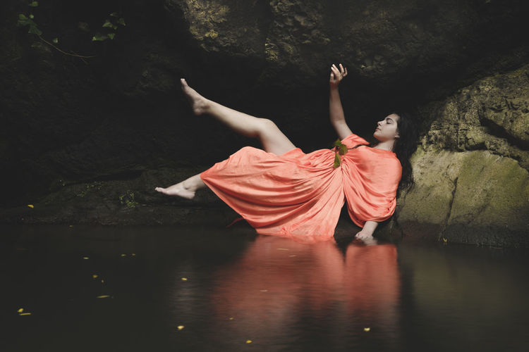 Woman wearing orange dress while lying on rock by lake