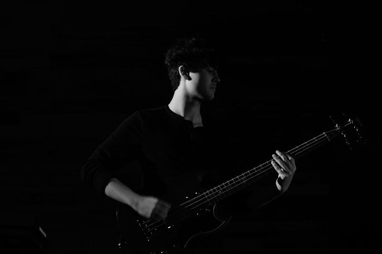 Man playing guitar while standing against black background