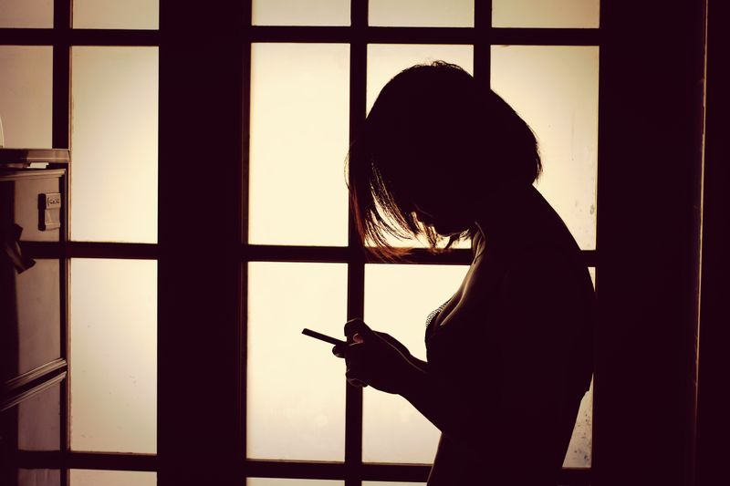 Silhouette woman looking through window at home