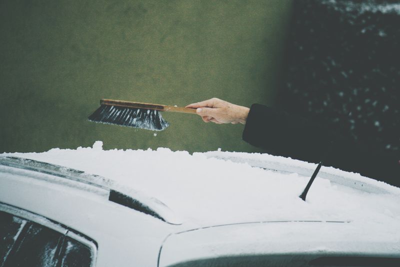 Eine männerhand kehrt mit einem besen den schnee vom weißen auto