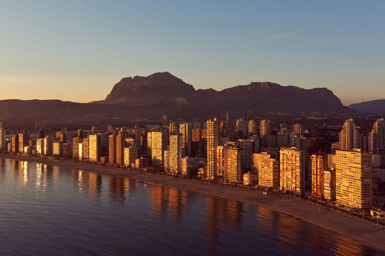 Aerial view of sea by city against sky at sunset