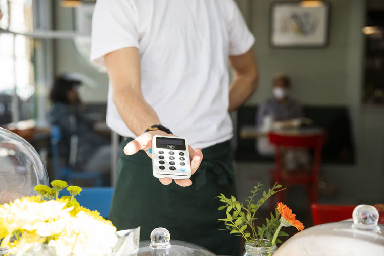 Male cafe owner showing credit card reader while standing in cafe