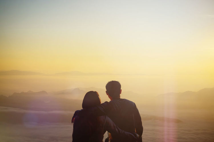 Rear view of couple sitting against sky during sunset