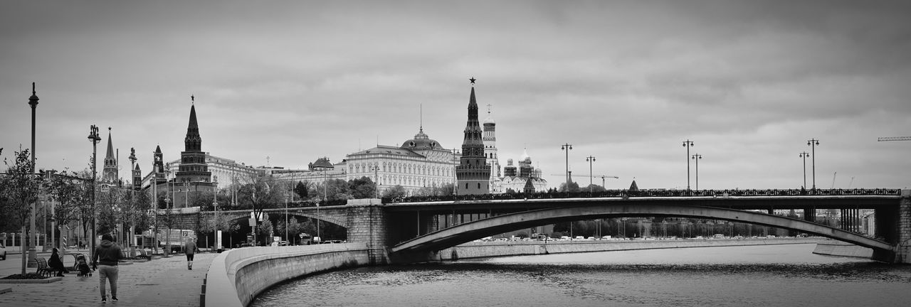 Bridge over river in city against cloudy sky