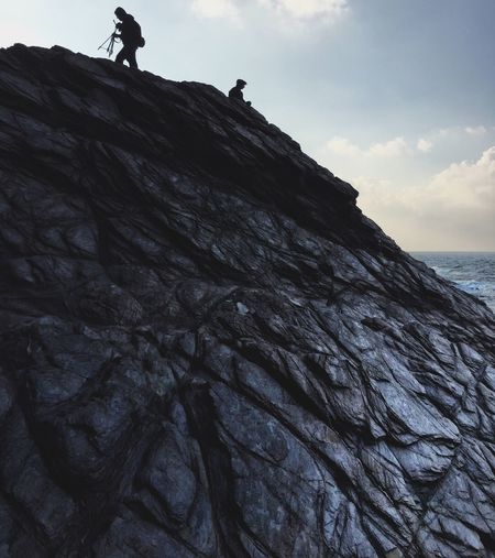 Low angle view of silhouette people on rock by sea against sky