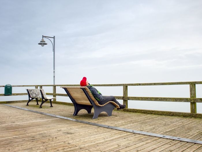 Man sitting on bench by wooden pier promenade, sea bridge at port
