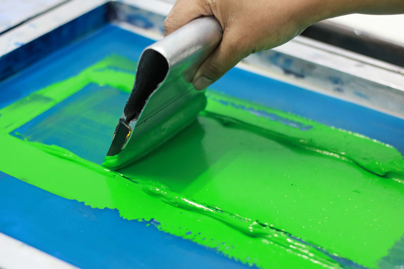 Cropped hand of person applying green ink on silk screen while working at workshop