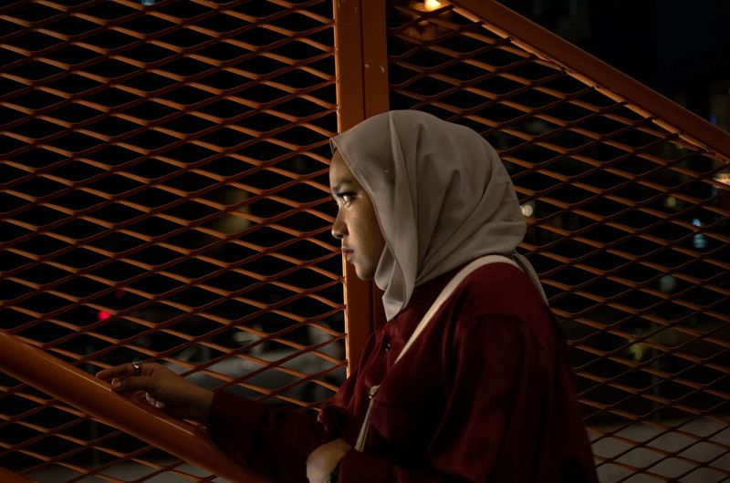 Woman in hijab looking away by chainlink fence