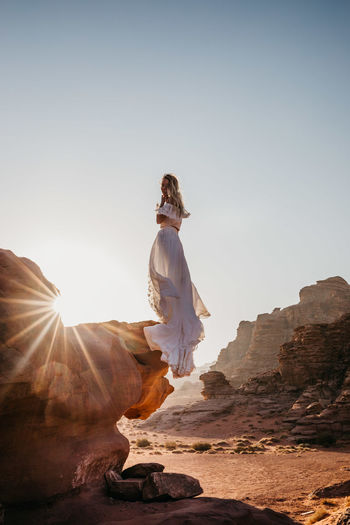 Woman in dress standing on rock against sky