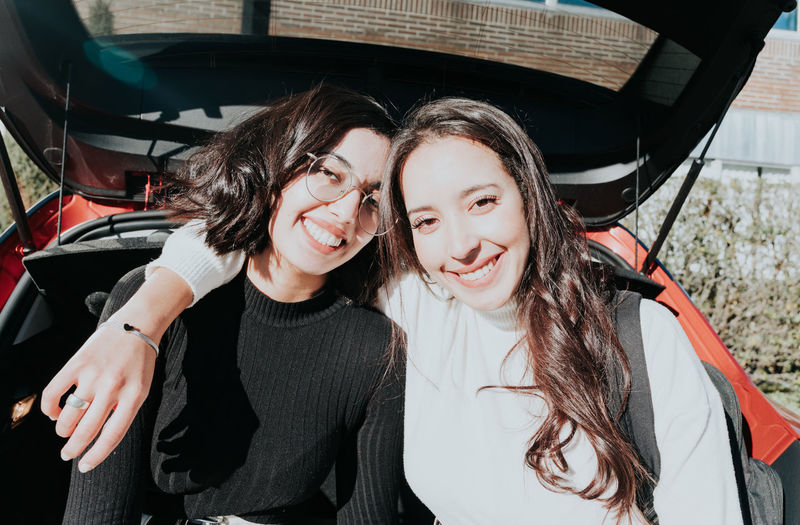 Portrait of smiling friends standing by car trunk