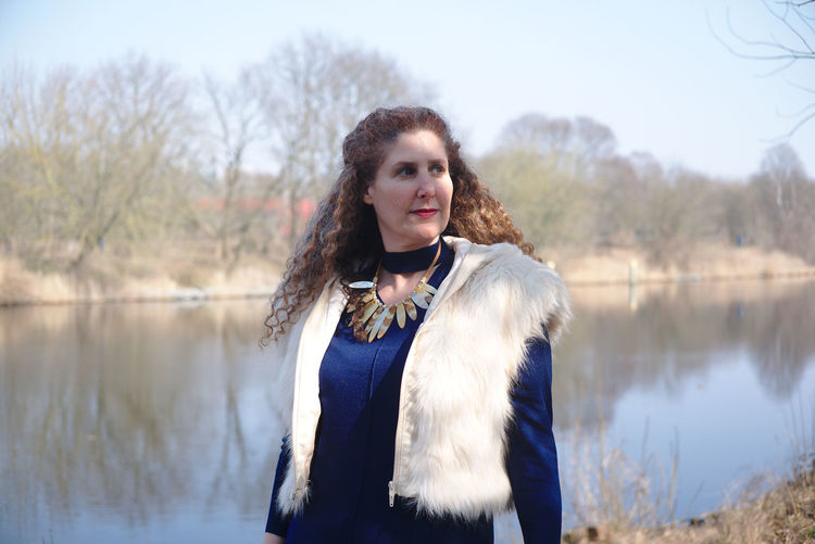 Mature woman wearing warm clothing while standing against lake