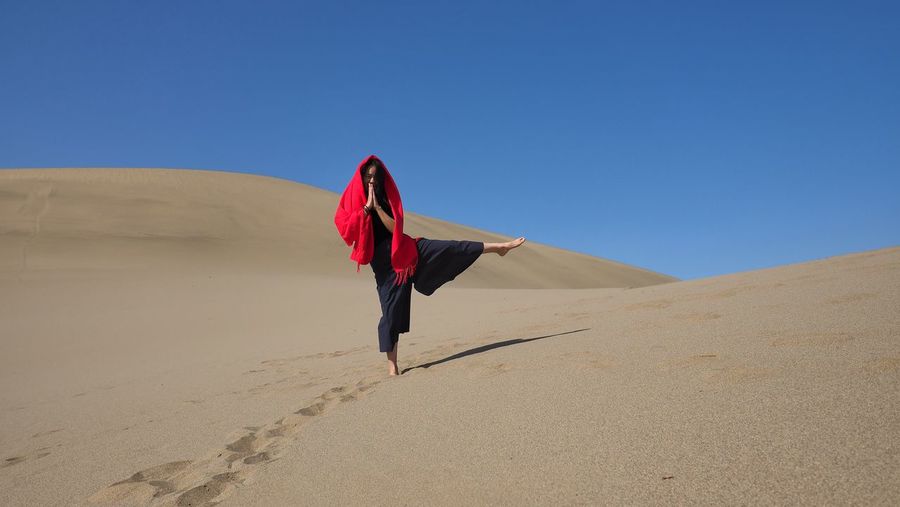 Full length of woman standing at desert against clear blue sky on sunny day