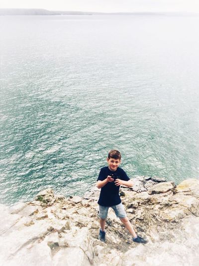 Boy standing on rock by sea