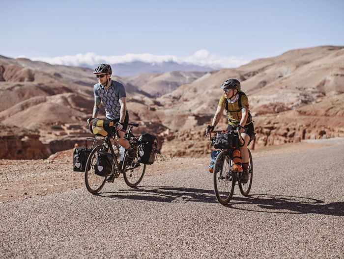 Two cyclists bike along remote mountain road in the desert of morocco