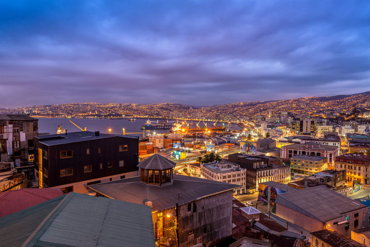 High angle view of sea and illuminated buildings against cloudy sky