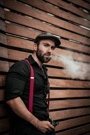 Portrait of young man smoking against wooden wall