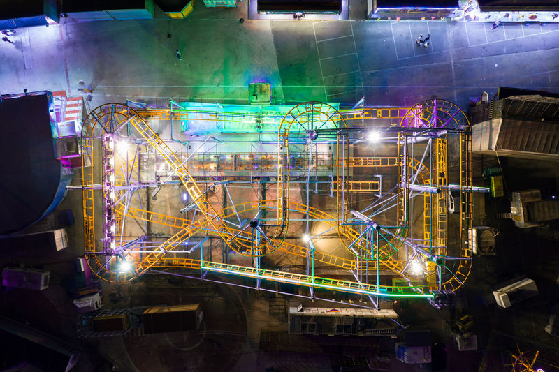 Drone view of roller coaster attraction located in public amusement park with bright glowing lights at night time in city