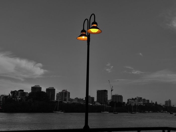 Illuminated street light in city against sky
